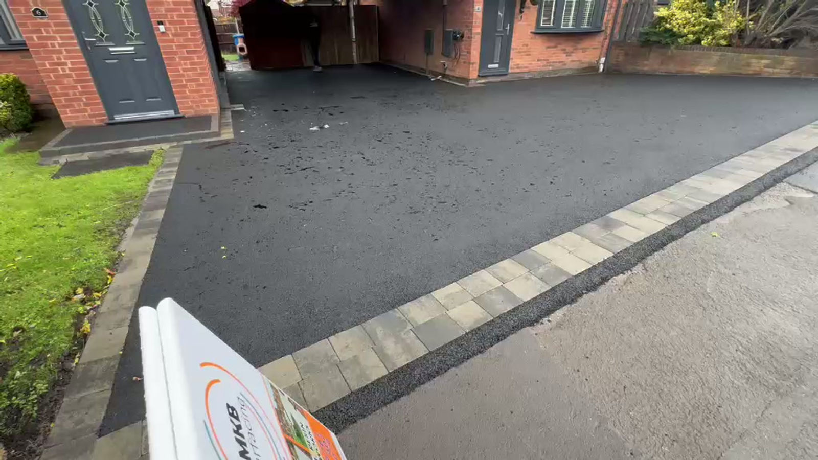 Black tarmac driveway edged with decorative patios at a brick house